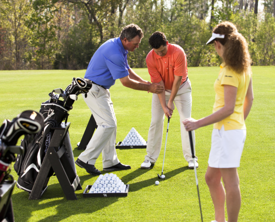 Instructor enseñando a un hombre y una mujer a jugar al golf